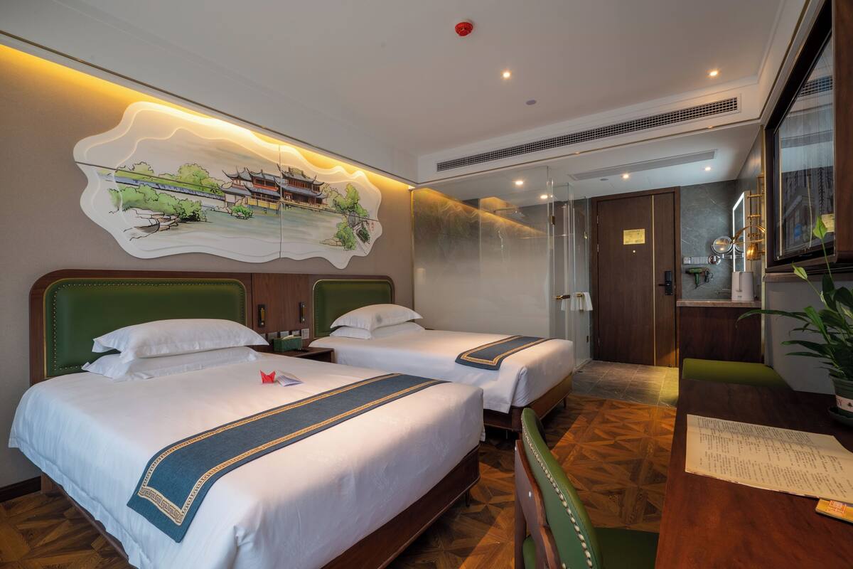 Ein Hotelzimmer mit zwei Betten, einem Esstisch, einem großen Spiegel und einem an der Wand hängenden Kunstwerk.