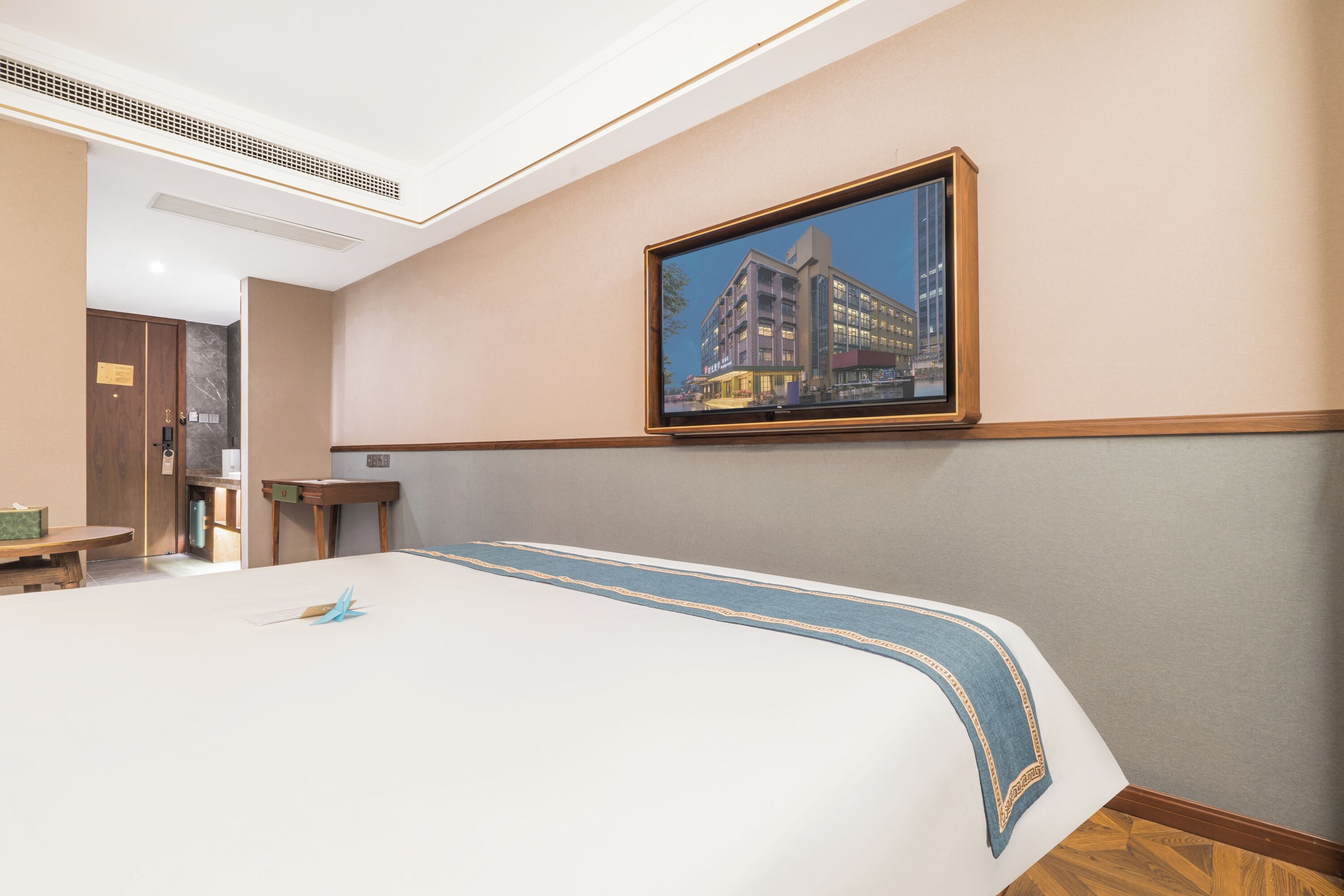 Hotellihuone, jossa on suuri sänky, seinällä kehystetty taulu ja pieni pöytä tuolilla.