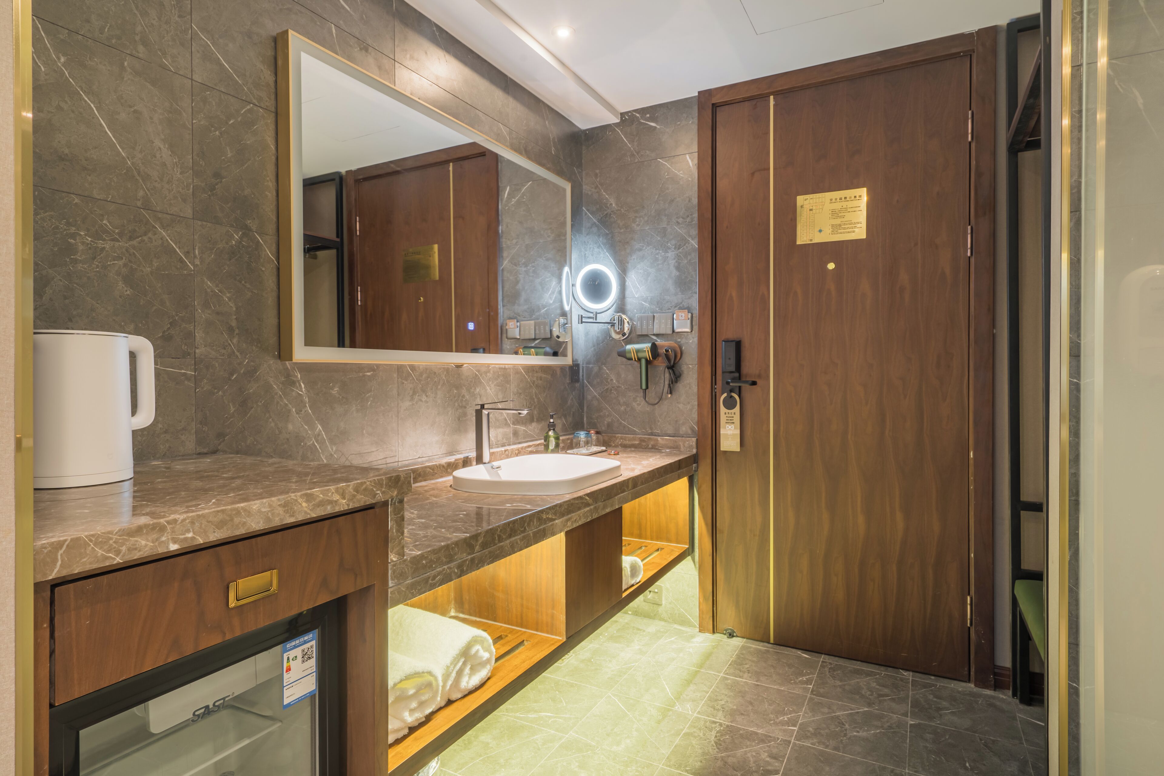 A modern bathroom with a marble countertop, a sink, a mirror with a ring light, and a wooden door.