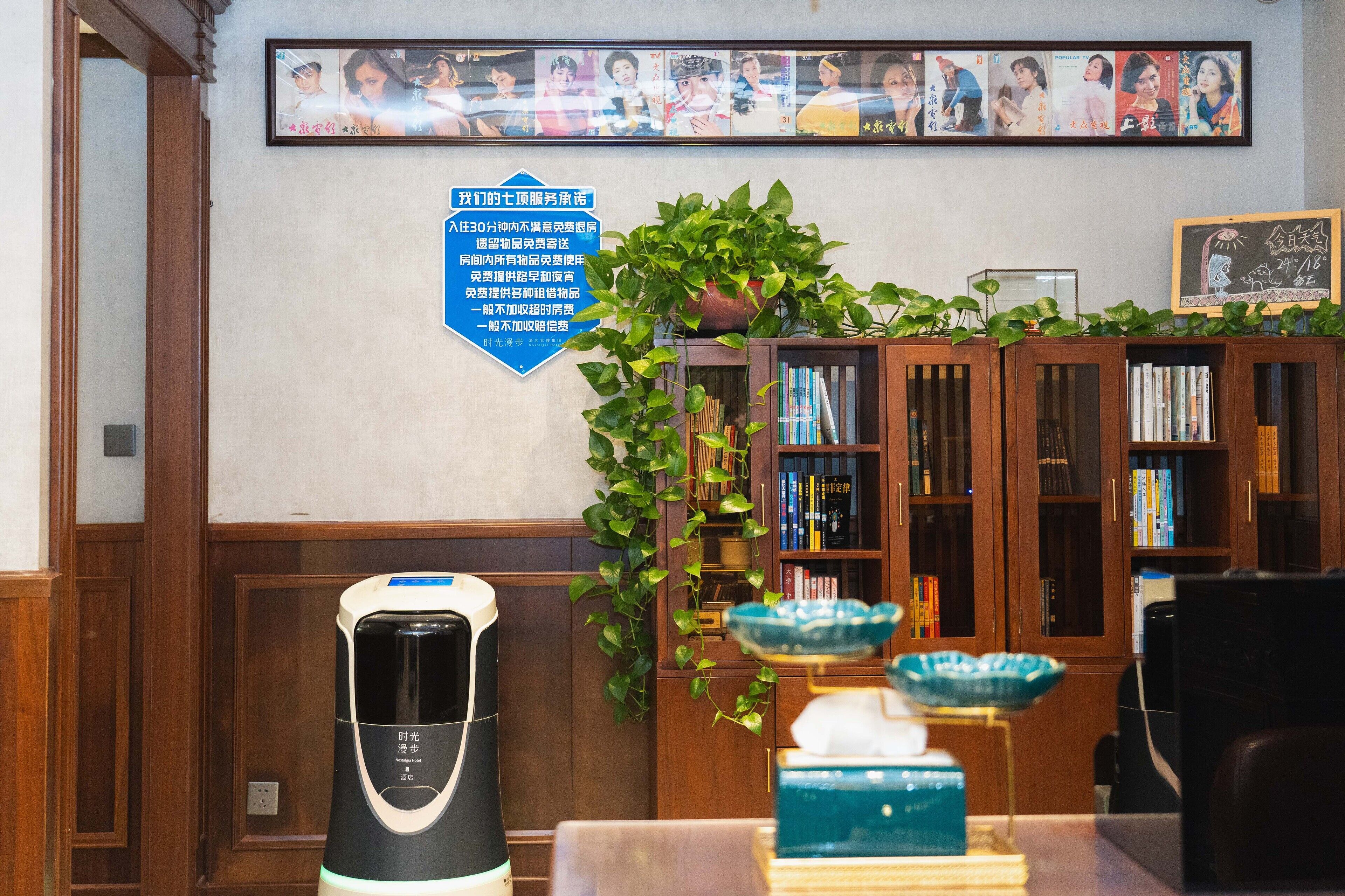 A room with a coffee maker, a bookshelf, and a framed photo on the wall.