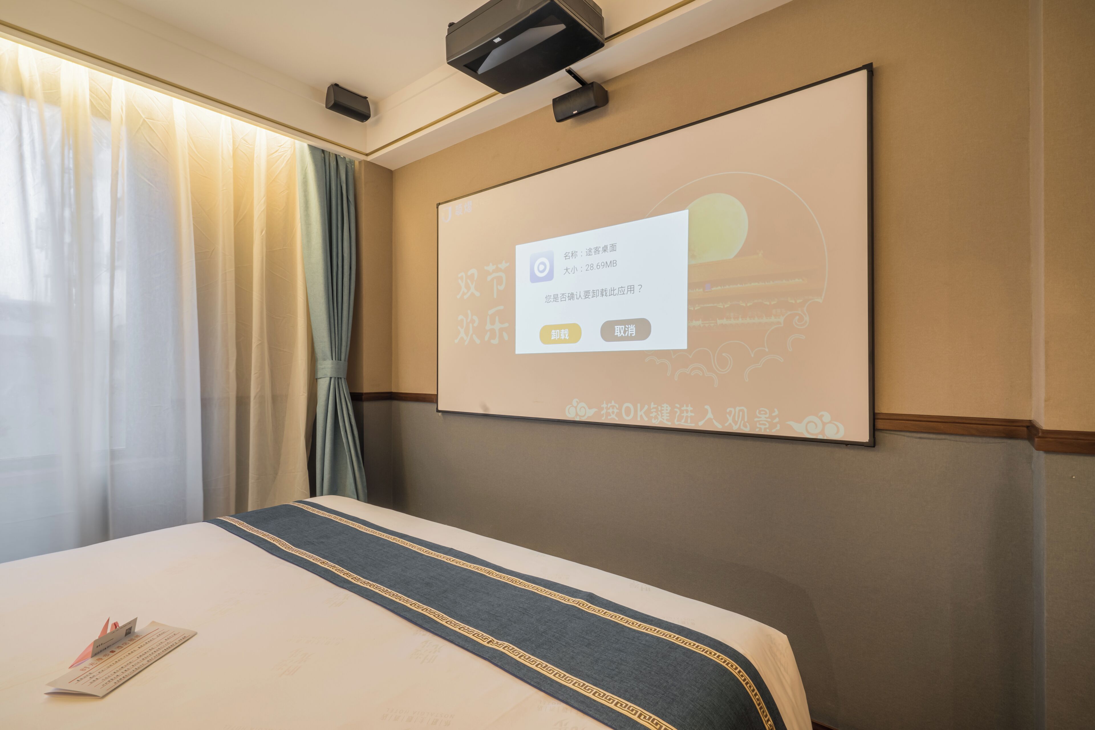 A hotel room with a bed, a projector screen displaying a message, and a window with curtains.