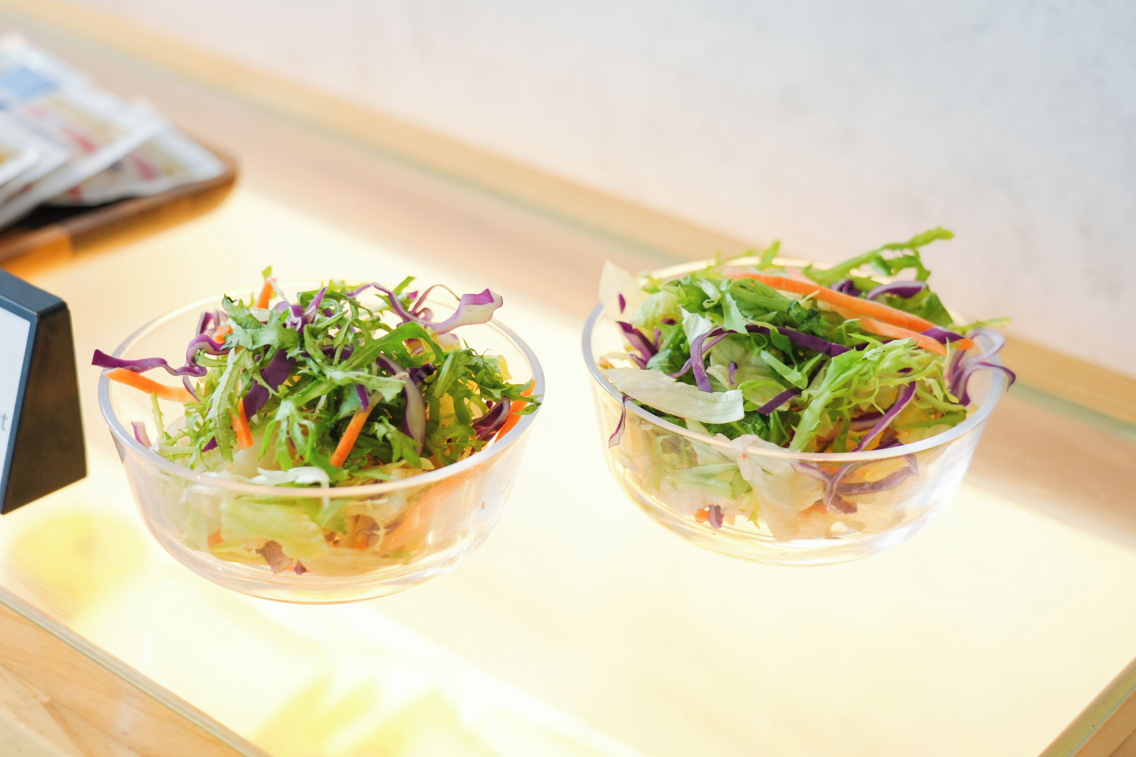 Two clear glass bowls of salad on a wooden surface.
