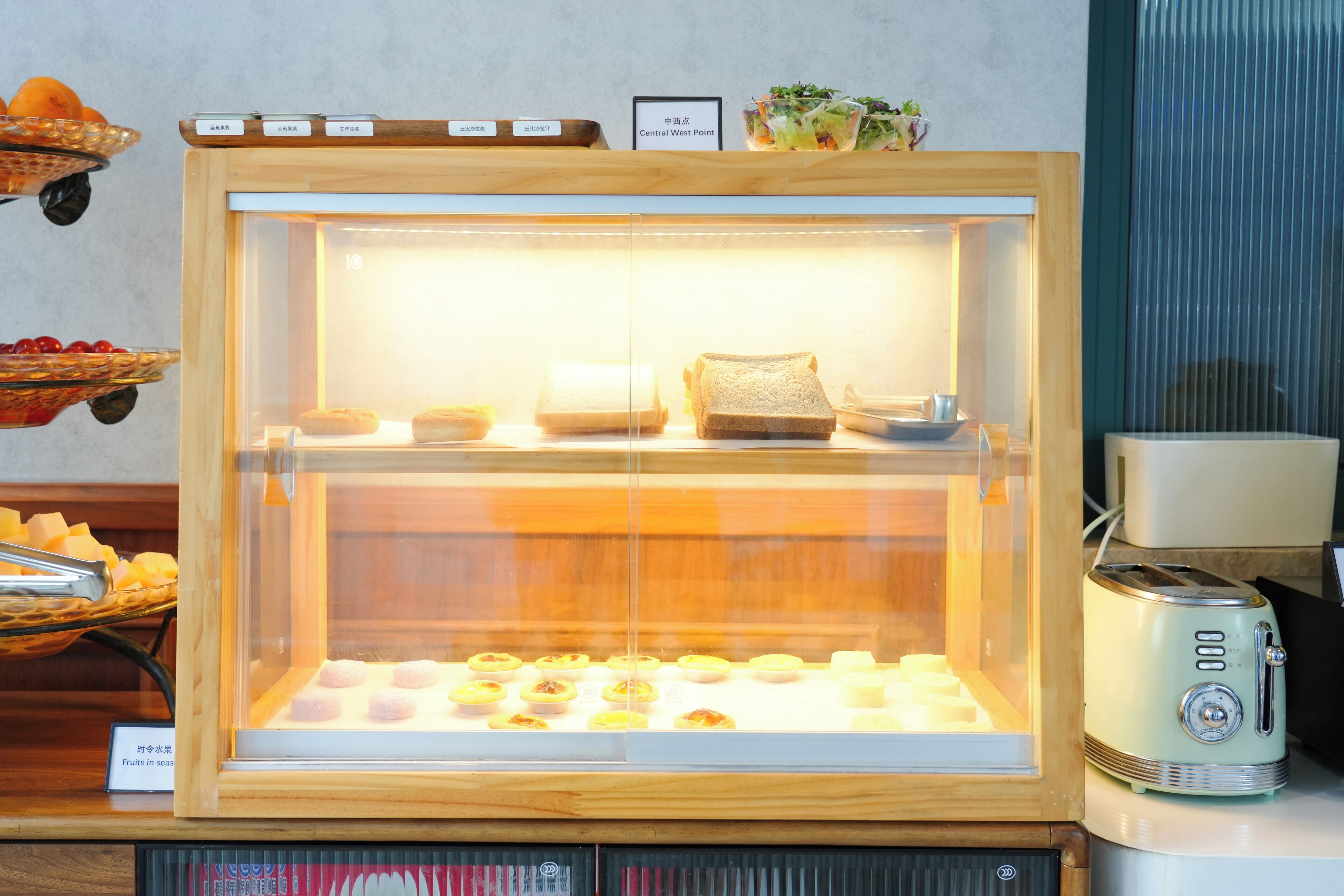 A bakery display case with pastries and bread, a toaster, and a fruit basket.
