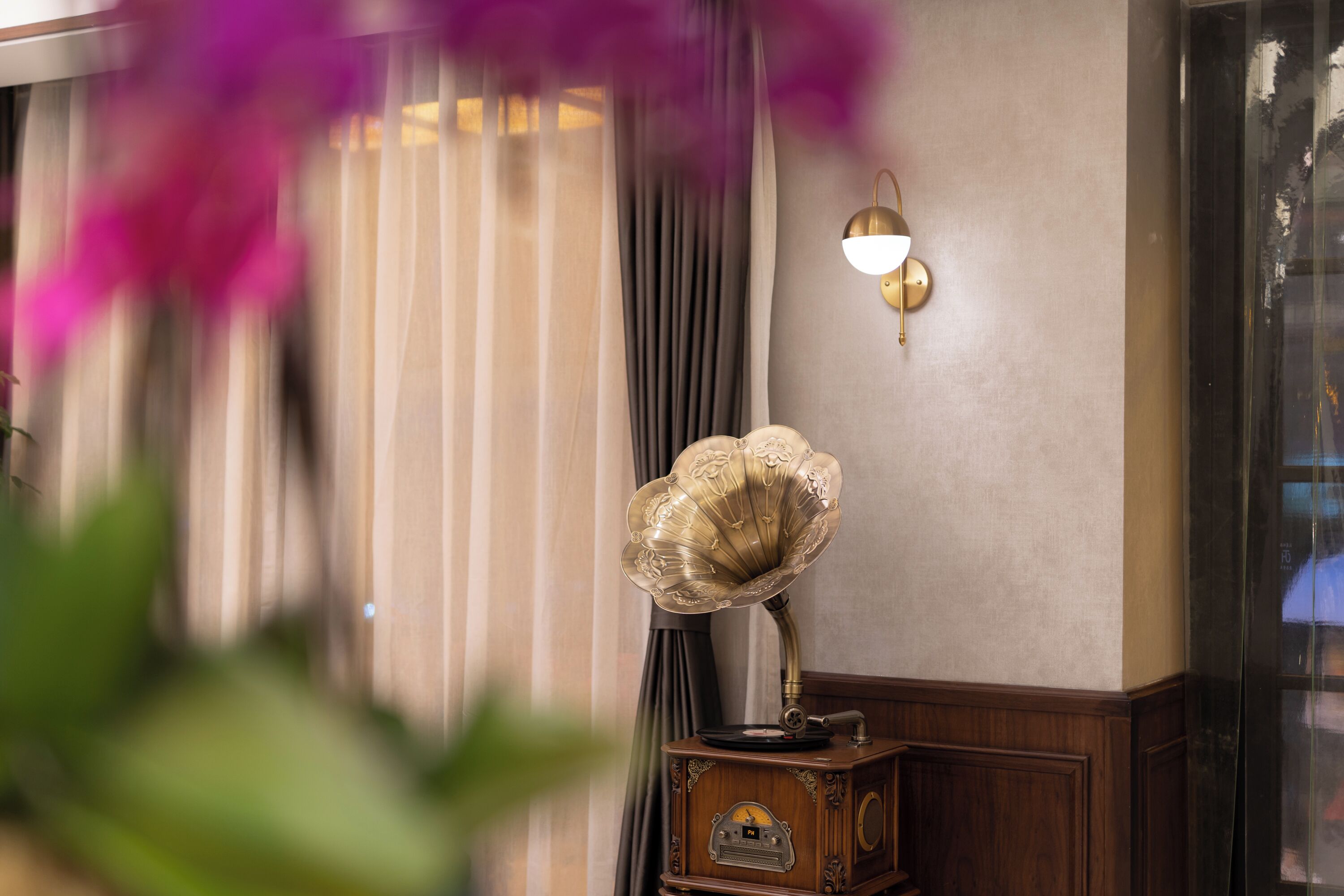 A vintage gramophone on a wooden table with a wall-mounted light fixture.