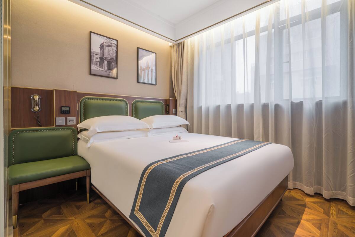 Ein Hotelzimmer mit einem großen Bett, einer grünen Bank, einem Telefon und zwei gerahmten Bildern an der Wand.