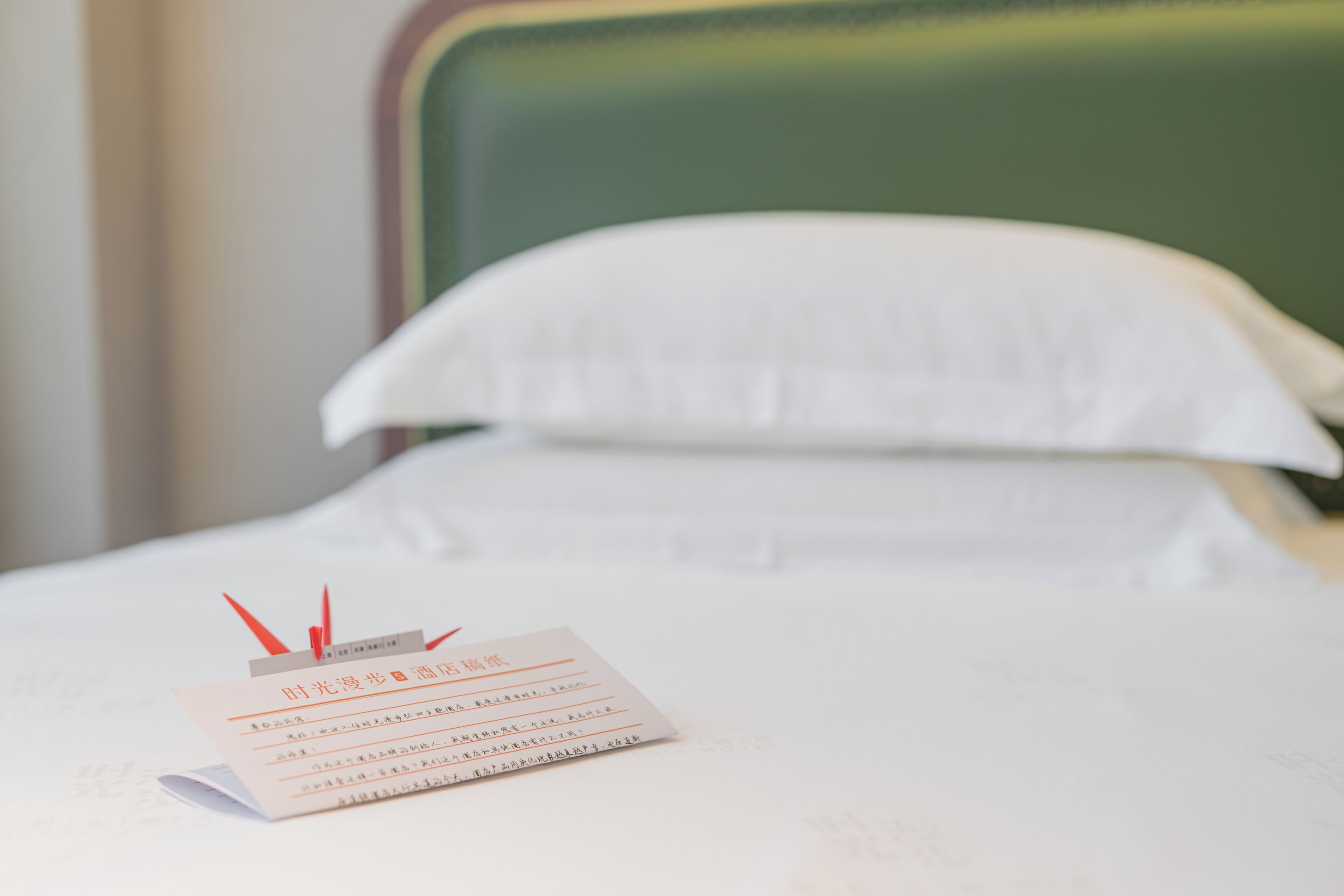 Un lit bien fait, avec des draps blancs et une feuille de papier pliée posée dessus.
