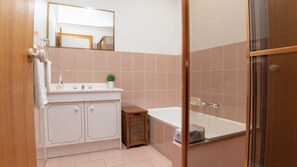A bathroom with a white vanity, a small wicker stool, a white bathtub, and a glass shower enclosure.