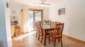 A dining area with a wooden table and chairs, a ceiling fan, a clock, and a painting on the wall.