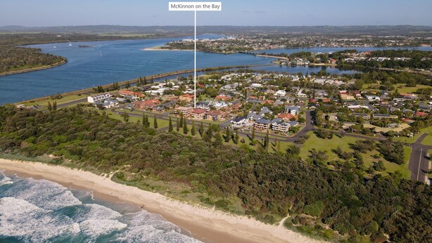 An aerial view of McKinnon on the Bay, featuring a coastal residential area with houses, roads, and a beach.