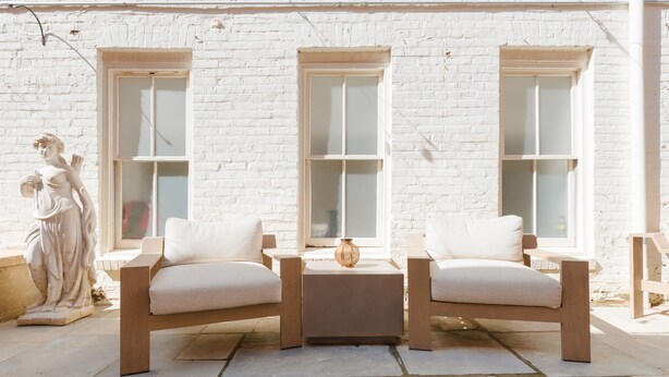 A patio with two white cushioned chairs, a small table, and a statue. There are three windows with white frames. - The King Street House by Kasa (Alexandria)