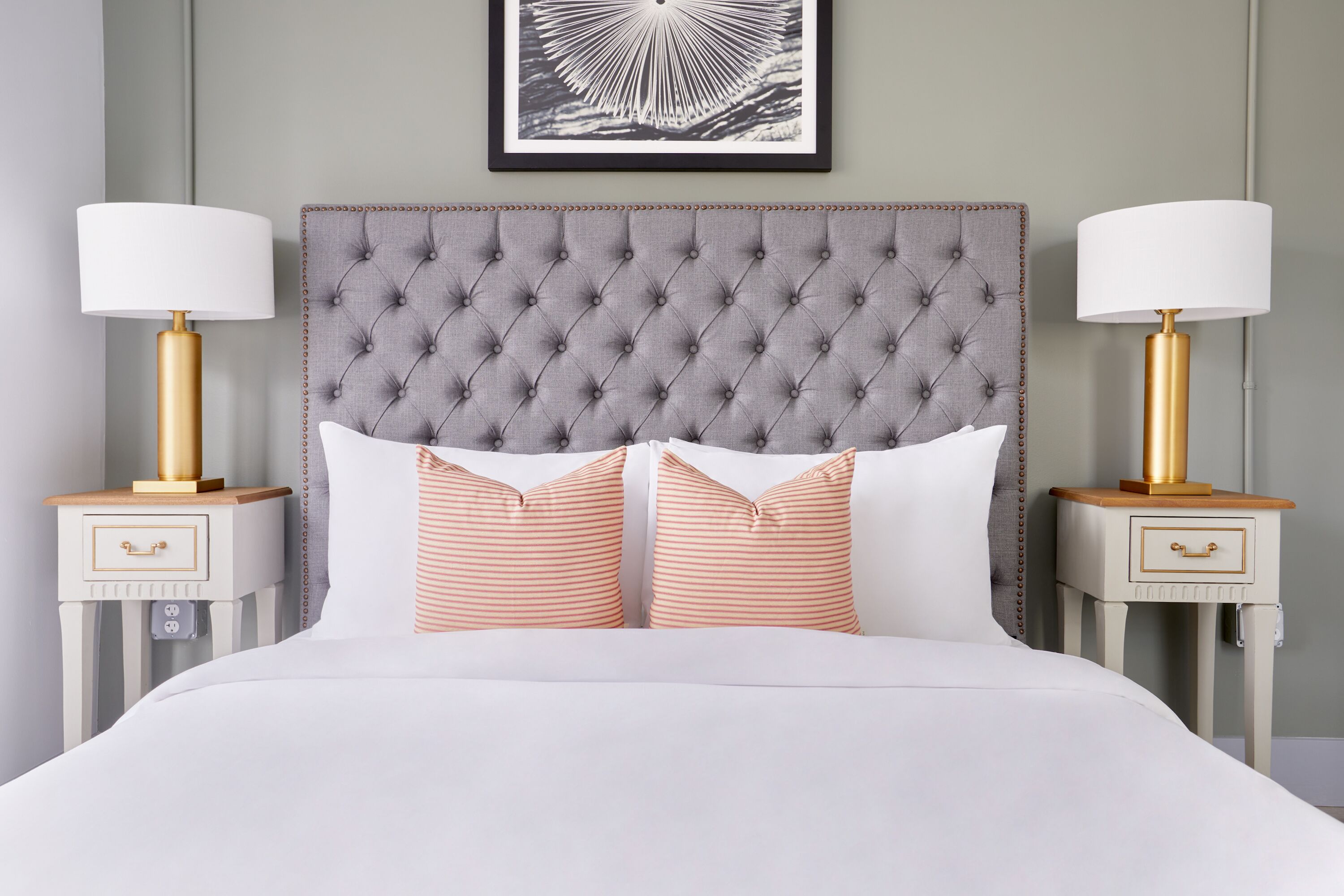 A neatly made bed with a tufted headboard, two bedside tables with lamps, and a framed artwork above the bed.