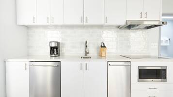 A modern kitchen with stainless steel appliances, white cabinetry, and a tiled backsplash.
