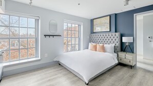 A bedroom with a large bed, two windows, a nightstand, and a wall-mounted shelf. - The King Street House by Kasa (Alexandria)