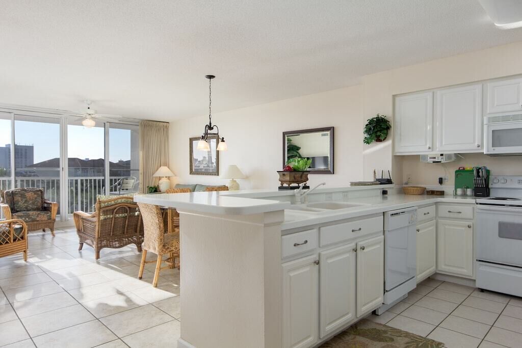 A modern kitchen with white cabinets, a large island, and a dining area with wicker furniture.