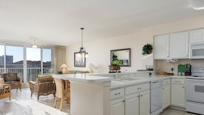 A modern kitchen with white cabinets, a large island, and a dining area with wicker furniture.