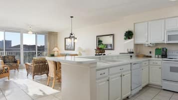 A modern kitchen with white cabinets, a large island, and a dining area with wicker furniture.