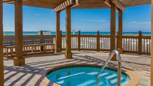 A wooden deck with a pool, benches, and a view of the beach.
