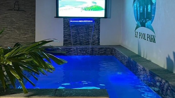 Ett poolområde med en konstgjord vattenfallskaskad, en tv-skärm och en väggmålning som föreställer ett hus.