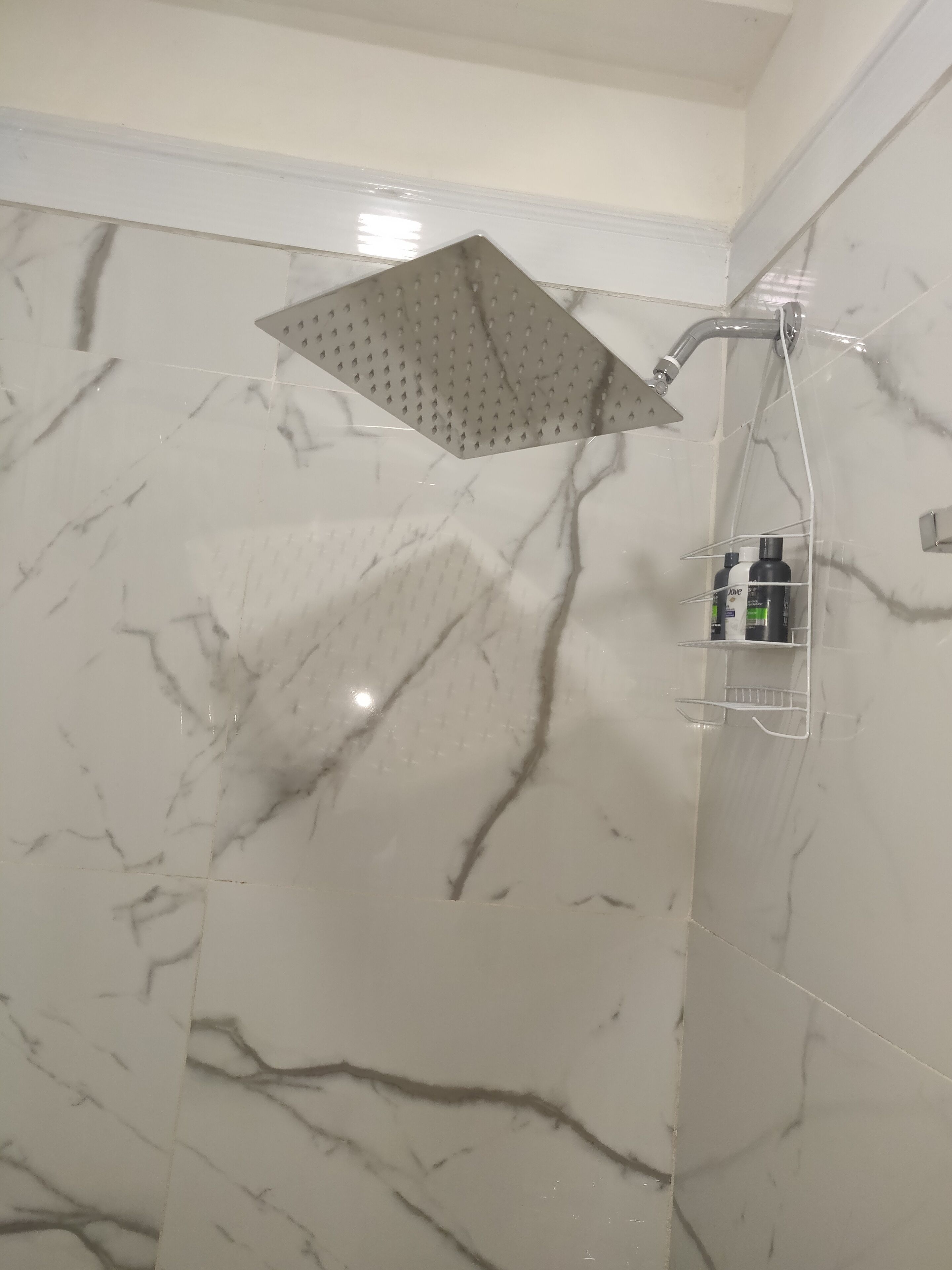 Une salle de bain avec une douche, des murs en marbre et une étagère contenant des articles de toilette.