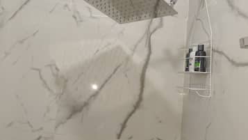 Une salle de bain avec une douche, des murs en marbre et une étagère contenant des articles de toilette.