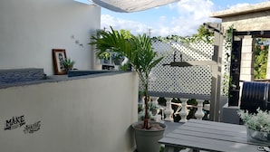 En uteplats med ett bord och stolar, en krukväxt och en vägg med en inramad bild och ett inspirerande citat.