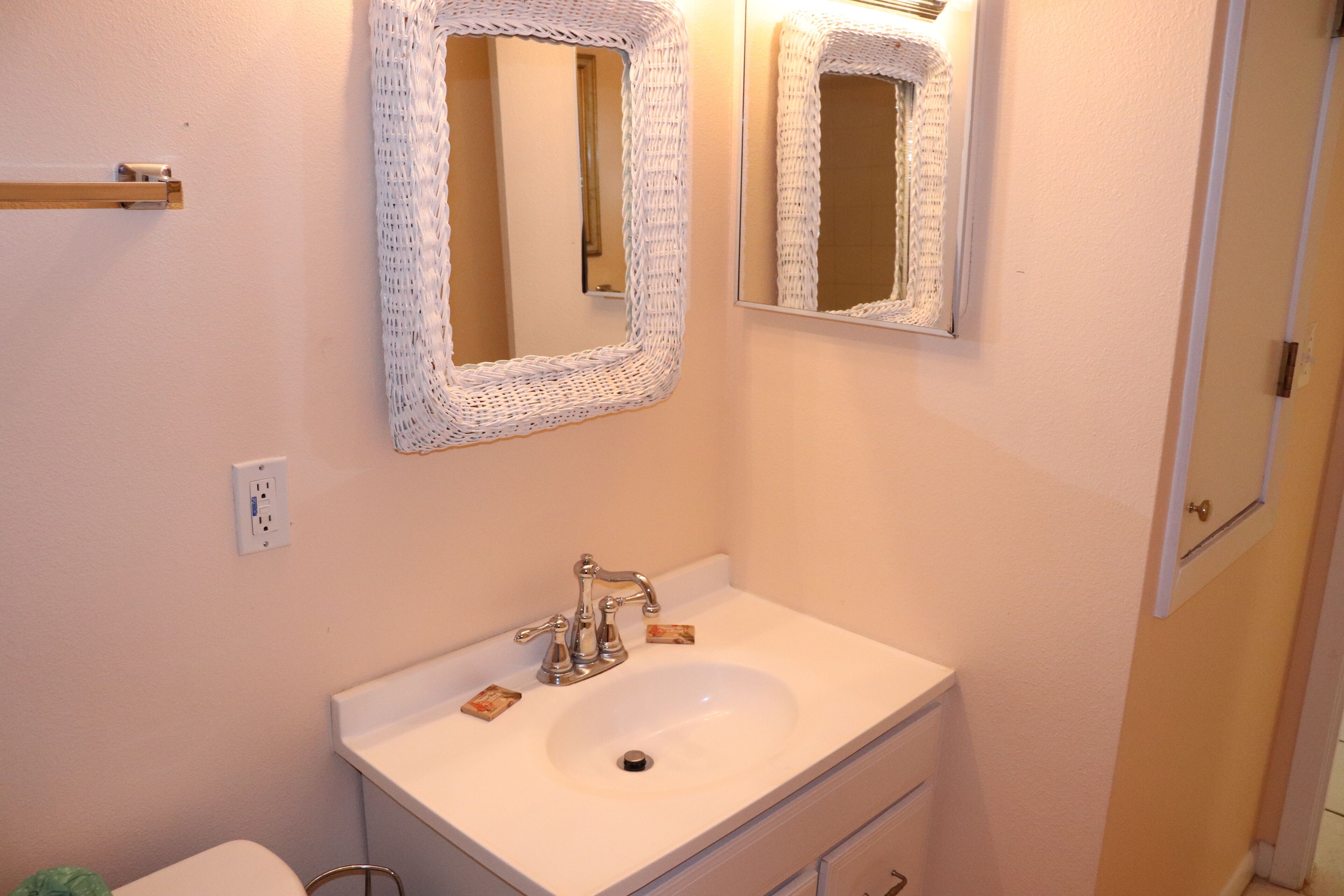 Une salle de bain avec un lavabo blanc, deux miroirs et un porte-serviettes en bois.
