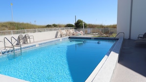 A rectangular swimming pool with a white tiled edge, a shallow end marked as 4 ft, and a deeper end marked as 7 ft. There are lounge chairs and a poolside table with a sign indicating pool rules.