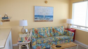 A living room with a floral sofa, a small table with a lamp, a chair, and a painting of seagulls on the wall.