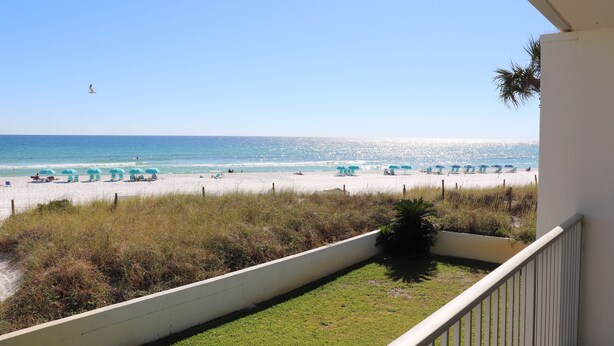 A balcony with a view of a beach with umbrellas and a clear sky.