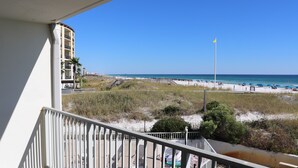 A balcony with a view of a beach, a flagpole, and a building in the background.