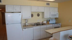 A compact kitchen with white cabinets, a refrigerator, a microwave, a sink, and a dishwasher.