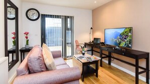 A modern living room with a sofa, a coffee table, a TV, and a window with blinds. - 15% Off Work Week Rates | 1Bd Apt w/Pvt Terrace (Cardiff)