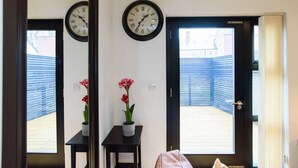 A room with two clocks on the wall, a small table with a potted plant, and a door leading to an outdoor area. - 15% Off Work Week Rates | 1Bd Apt w/Pvt Terrace (Cardiff)