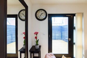 Una habitación con dos relojes en la pared, una pequeña mesa con una planta en maceta y una puerta que da a un espacio exterior.