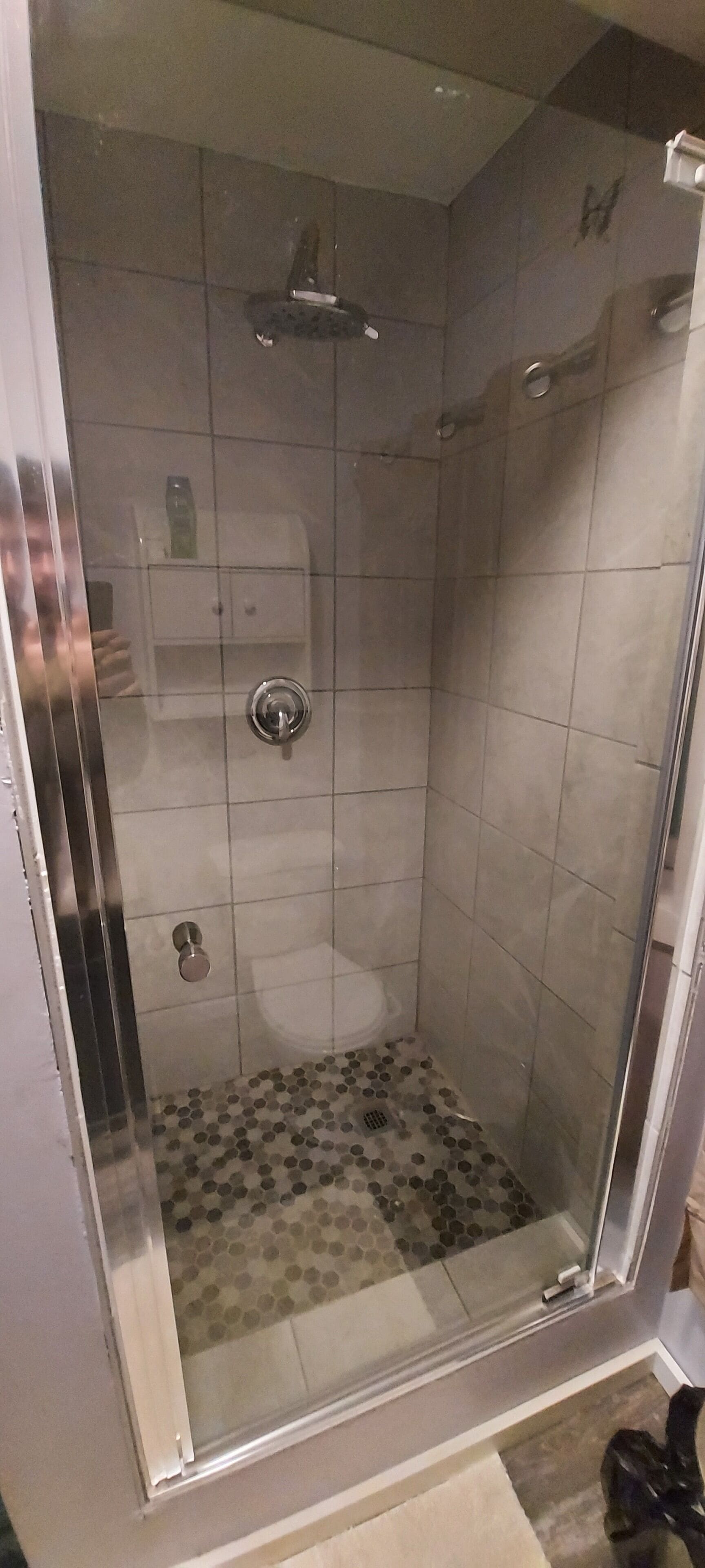 Une douche avec une porte en verre, des toilettes blanches et un sol carrelé.