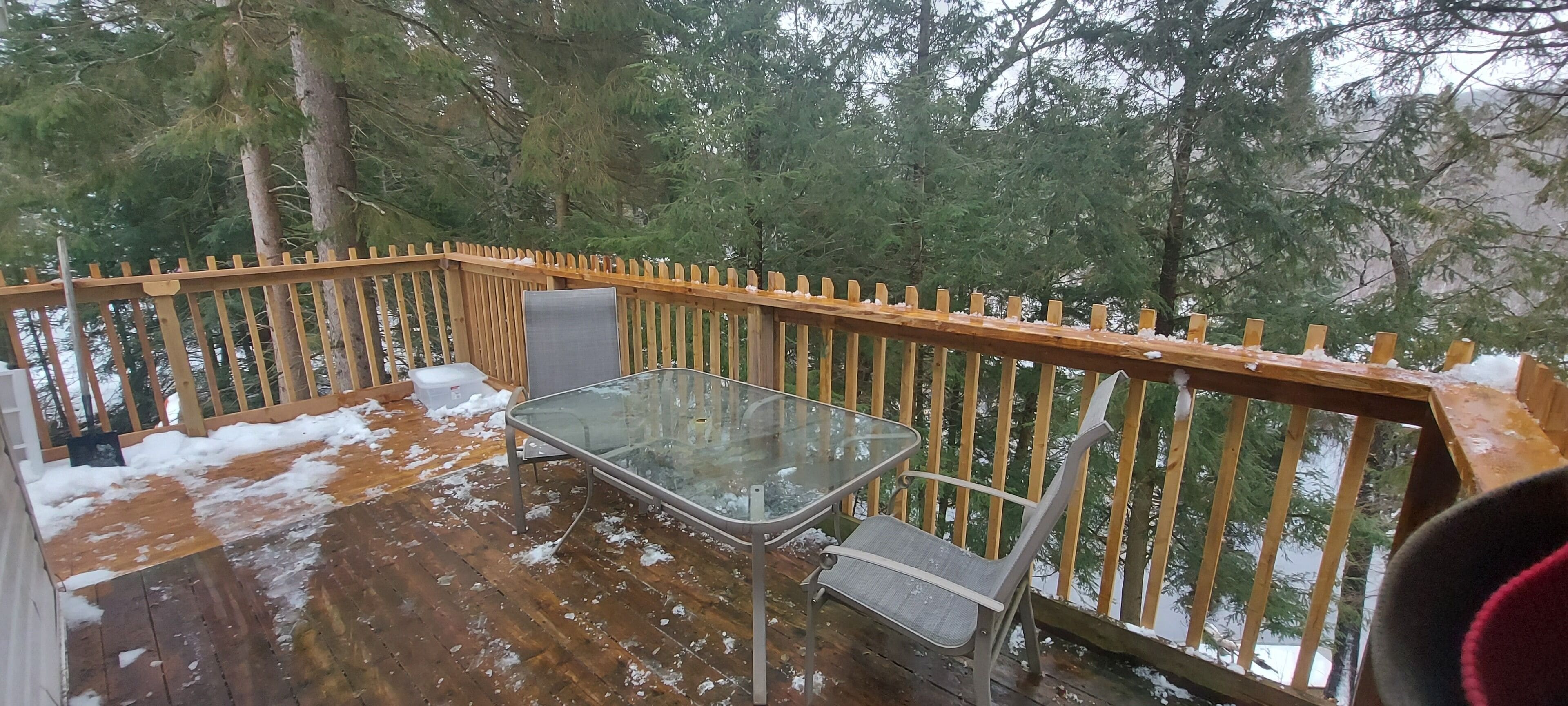 Eine Holzterrasse mit einem Glastisch und zwei Stühlen, umgeben von einem Holzgeländer.