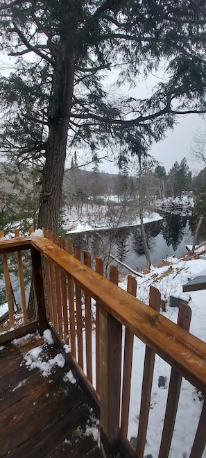 A wooden deck with a railing overlooking a snowy landscape with trees and a body of water. - Semi rural loft getaway on the river (Katrine)