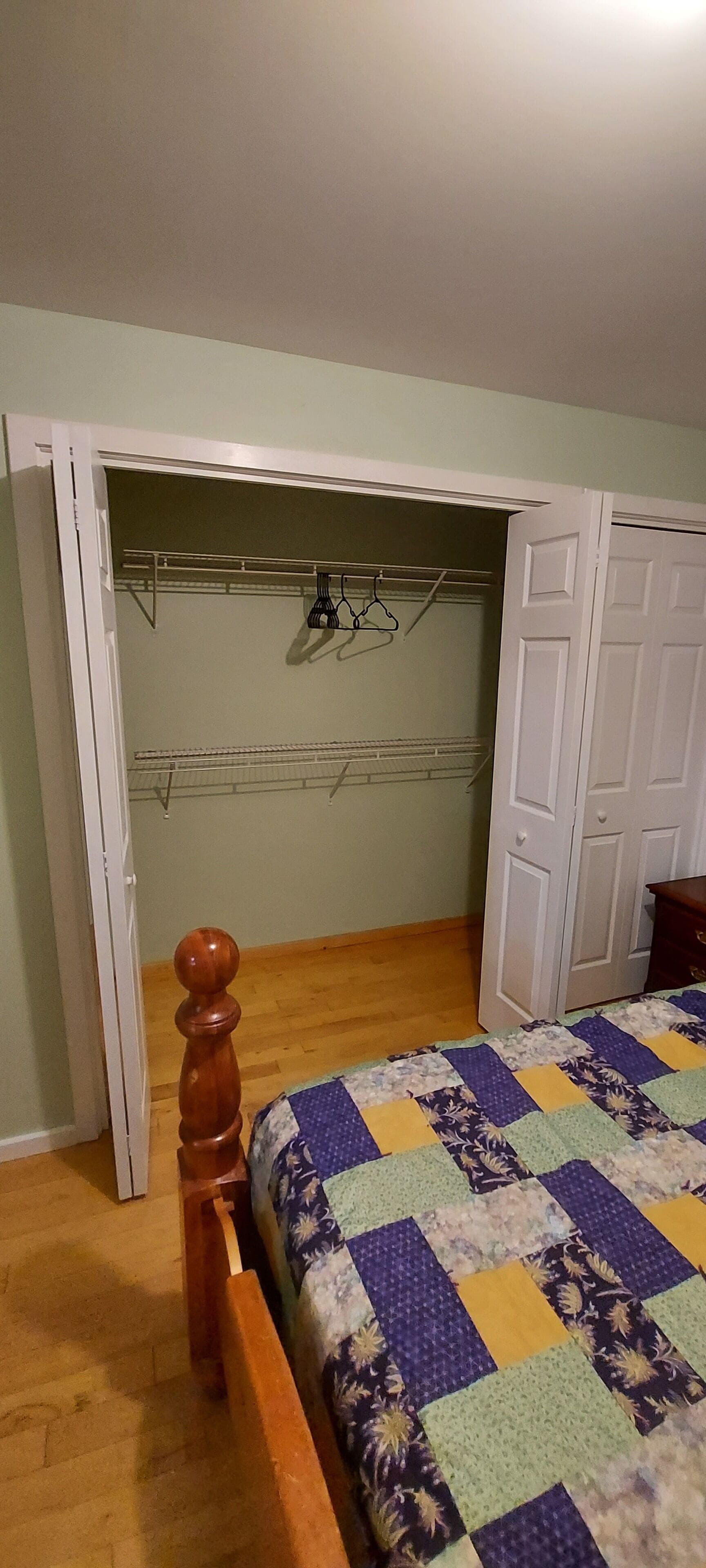 A bedroom with a bed, a wooden headboard, a closet, and a drying rack.
