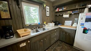A kitchen with wooden cabinets, a double sink, a coffee maker, a refrigerator, and a window with a view of trees. - House in Bessemer - 3 BR/1.5 Bathrooms (Bessemer)