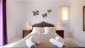 A neatly made bed with white linens and towels, a wooden headboard, two bedside tables with lamps, and butterfly wall art. - Nautilus Villa with private pool (Hersonissos)