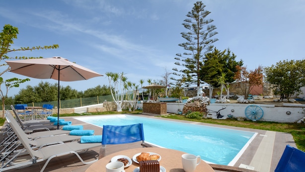 A poolside area with lounge chairs, a table with a cake and coffee cups, and a large umbrella. - Nautilus Villa with private pool (Hersonissos)