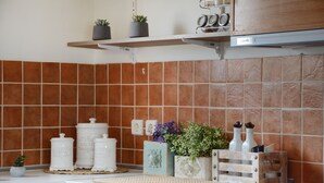 A kitchen with brown tiles, white cabinets, and a shelf with plants and kitchenware. - Nautilus Villa with private pool (Hersonissos)