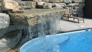 Une piscine agrémentée d’une cascade, entourée de murs en pierre et dotée d’un espace de détente avec des fauteuils.