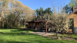 Eine Holzhütte mit überdachter Veranda, umgeben von einem gepflegten Rasen und Bäumen.