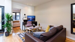 Un salón moderno con un sofá de cuero marrón, una mesa de centro, un escritorio con computadora y silla, un televisor de pantalla plana grande y una planta en maceta.