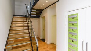 Una escalera de madera con barandillas de vidrio que conduce a un rellano con un mueble de almacenamiento verde.