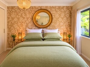A bedroom with a large bed, a round mirror, two bedside tables with lamps, and a window with curtains.