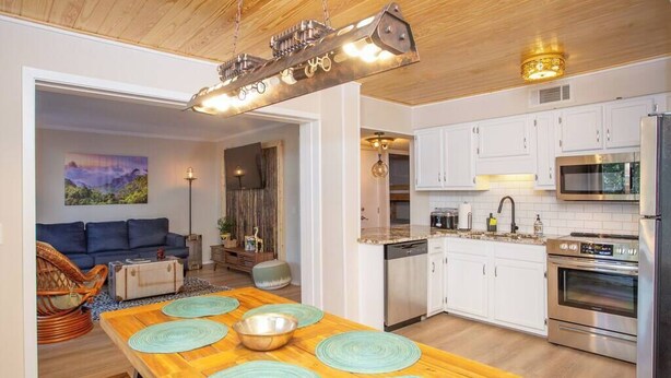 A modern kitchen with white cabinets, stainless steel appliances, and a wooden dining table with teal placemats.