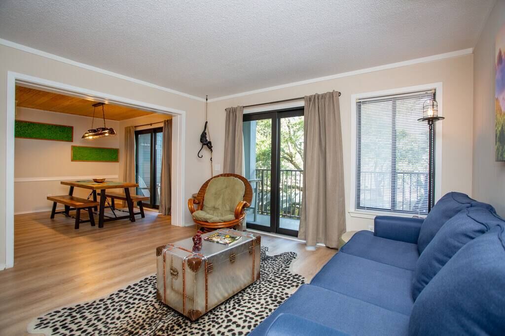 Un salon avec un canapé bleu, une table à manger en bois, un fauteuil vert et une valise ancienne.