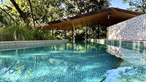 Una piscina de azulejos azules cristalinos, con un toldo de madera y una pared de piedra con un diseño geométrico.